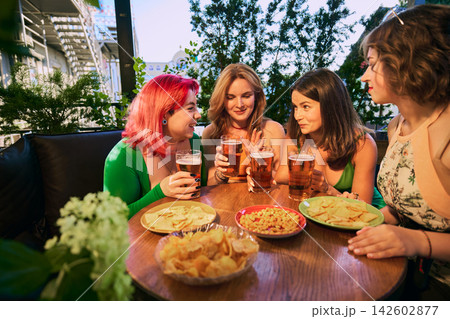 Smiling friends hold beer glasses above table with pizza and crunchy snacks Smiling friends hold beer glasses above table with pizza and crunchy snacks 142602877
