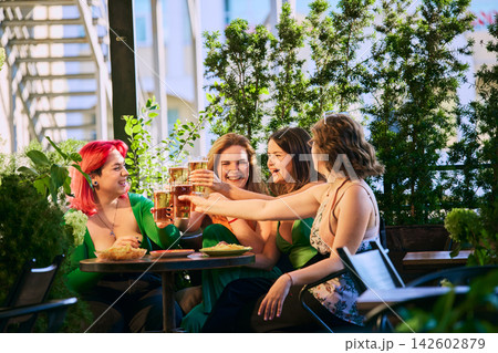 Women clink beer glasses while celebrating together on sunny patio Women clink beer glasses while celebrating together on sunny patio 142602879