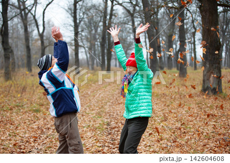 Elderly couple throws up fallen leaves in the forest during the autumn season Elderly couple throws up fallen leaves in the forest during the autumn season 142604608