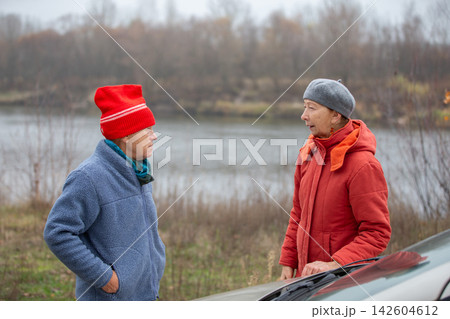 An elderly couple talking on the river bank in a natural setting on a cool autumn day under a cloudy sky. 142604612