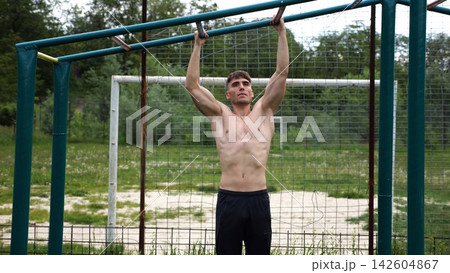 Young muscular sportsman doing pull ups at sports ground. Athletic guy exercising outdoor. Strong sporty man working out at summer nature. Concept of healthy and active lifestyle. Slow motion Young muscular sportsman doing pull ups at sports ground. Athletic guy exercising outdoor. Strong sporty man working out at summer nature. Concept of healthy and active lifestyle. Slow motion 142604867