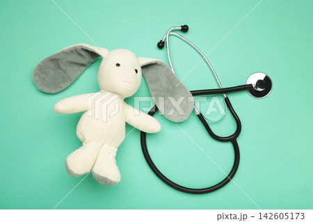 Pediatrician concept. Toy bunny and stethoscope on mint background. Pediatrician concept. Toy bunny and stethoscope on mint background. 142605173