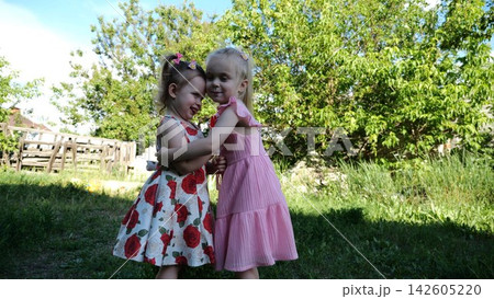 Two cute little sisters hugging each other tightly on green grass outdoor. Beautiful small girls smiling and embracing in summer garden on sunny day. Carefree children show family love and friendship Two cute little sisters hugging each other tightly on green grass outdoor. Beautiful small girls smiling and embracing in summer garden on sunny day. Carefree children show family love and friendship 142605220