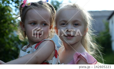 Portrait of two cute little girls in a summer garden. Beautiful happy sisters looking into camera on a bright sunny day. Innocent small children with joyful faces enjoying childhood moments in nature Portrait of two cute little girls in a summer garden. Beautiful happy sisters looking into camera on a bright sunny day. Innocent small children with joyful faces enjoying childhood moments in nature 142605221