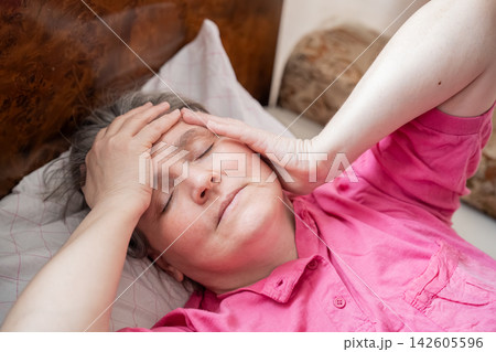 Mature woman resting in bed with hands on her forehead at home. Menopause awareness headache fatigue discomfort and recovery 142605596