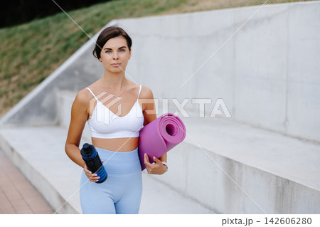 Young woman holding yoga mat and water bottle going to fitness training Young woman holding yoga mat and water bottle going to fitness training 142606280