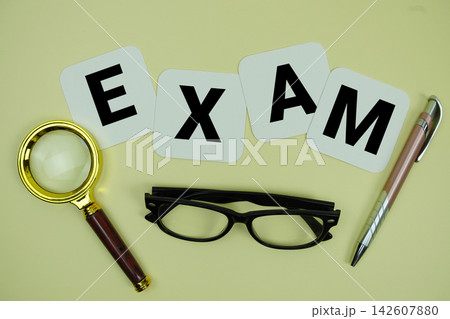 EXAM alphabet letters with magnifying glass, eye glasses and pen on yellow background EXAM alphabet letters with magnifying glass, eye glasses and pen on yellow background 142607880