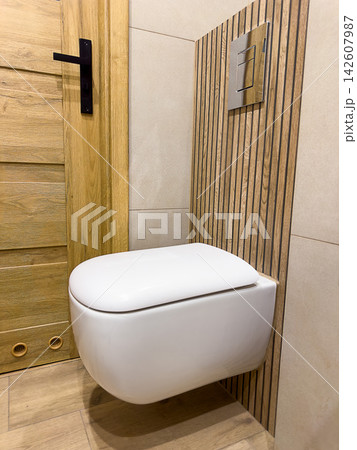 Wall hung toilet installation in modern bathroom with flush plate, wood tiles, plumbing, hygiene and interior renovation Wall hung toilet installation in modern bathroom with flush plate, wood tiles, plumbing, hygiene and interior renovation 142607987
