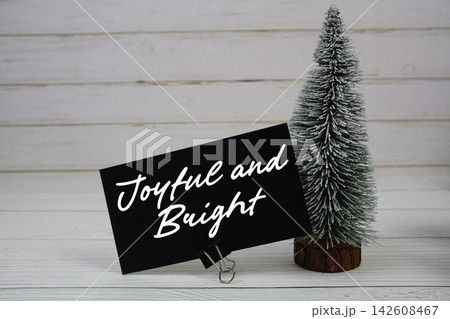 Joyful and Bright text written on paper card with snowy tree on wooden background Joyful and Bright text written on paper card with snowy tree on wooden background 142608467