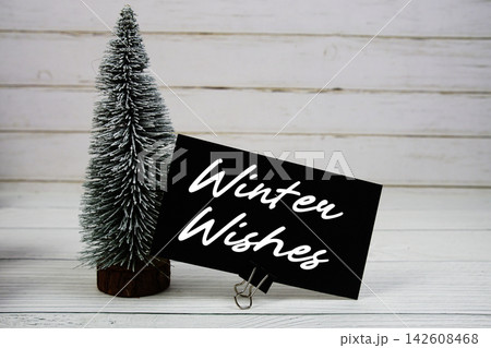 Winter Wishes text written on paper card with snowy tree on wooden background Winter Wishes text written on paper card with snowy tree on wooden background 142608468
