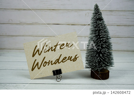 Winter Wonders text written on paper card with snowy tree on wooden background Winter Wonders text written on paper card with snowy tree on wooden background 142608472