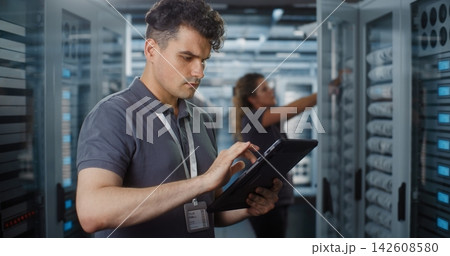 Male IT Specialist Using Tablet while Female Engineer Inspects Server Rack Male IT Specialist Using Tablet while Female Engineer Inspects Server Rack 142608580