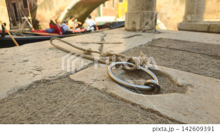 Metal mooring ring and rope sit beside a gondola on a canal in Venice, Italy. Concepts: Venetian travel, maritime heritage, transportation, tourism, traditional boating, urban waterways. 142609391