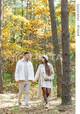 A pregnant woman and her partner stroll hand-in-hand through a sun-dappled forest, enjoying the fall colors A pregnant woman and her partner stroll hand-in-hand through a sun-dappled forest, enjoying the fall colors 142610302