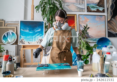 Female artist shaping fluid epoxy resin with wooden spatula to create pattern on abstract painting. Female artist shaping fluid epoxy resin with wooden spatula to create pattern on abstract painting. 142611531