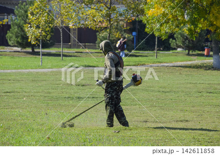 worker mowing grass with a gasoline brush. Trimmer. worker mowing grass with a gasoline brush. Trimmer. 142611858