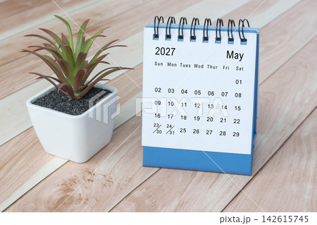 May 2027 desk calendar with potted plant on wooden desk. 142615745