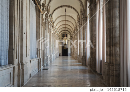 Sunlit arched gallery with royal statue and visitors walking through a palace corridor 142618713