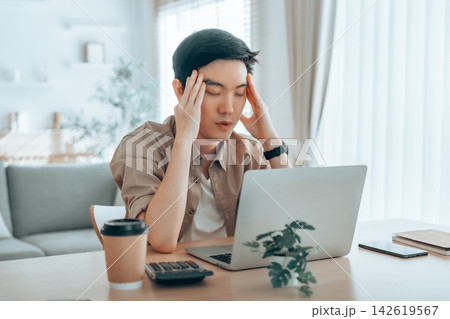 Asian man are stressed, pain in their eyes, working on laptop in living room at home Asian man are stressed, pain in their eyes, working on laptop in living room at home 142619567