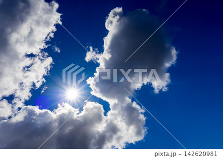 radiant sun beaming beside dramatic white clouds in a clear blue sky radiant sun beaming beside dramatic white clouds in a clear blue sky 142620981