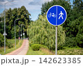 Sign shows bicycle and pedestrian path along a green area on a sunny day 142623385