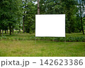 Billboard mockup stands in a green field surrounded by trees 142623386