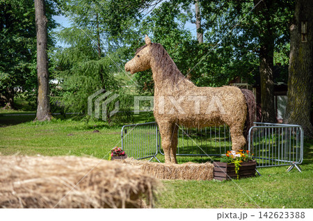 Straw horse sculpture stands in a park surrounded by trees during sunny daytime 142623388