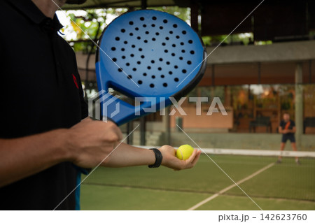 Player holds a padel ball in one hand while readying a racket 142623760