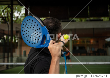 Player holds a padel racket ready to serve a bright yellow ball 142623761