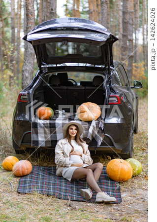 A beautiful pregnant woman is enjoying a fall day with pumpkins and a car in the forest A beautiful pregnant woman is enjoying a fall day with pumpkins and a car in the forest 142624026