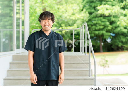 緑を背景に笑顔で立つ男性理学療法士・リハビリ医療を支える専門スタッフ 緑を背景に笑顔で立つ男性理学療法士・リハビリ医療を支える専門スタッフ 142624199