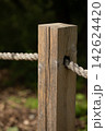 Weathered, textured rustic wooden fence post with thick rope on a blurred natural green background 142624420