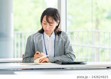 ノートを確認しながら仕事を振り返る女性スタッフ・研修や業務記録を見直すシーン ノートを確認しながら仕事を振り返る女性スタッフ・研修や業務記録を見直すシーン 142624825