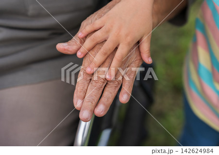 close up of senior and child holding hands on wheelchair armrest 142624984
