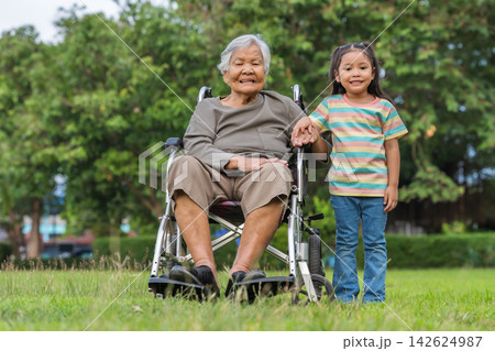 little child girl holding hand of grandmother sitting on wheelchair outdoors in park 142624987