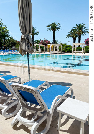 Empty sunbeds and umbrellas on pool terrace at spa resort exterior on cloudy day 142625240