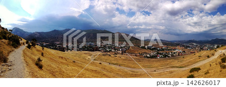 panorama of a valley with a town, mountain range, dirt path and dramatic clouds in sky panorama of a valley with a town, mountain range, dirt path and dramatic clouds in sky 142626017