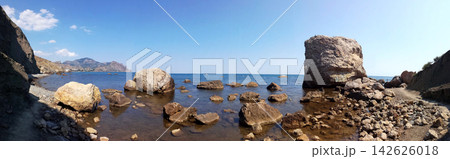 panoramic view of a rocky sea coast with massive boulders near water under a clear blue sky 142626018