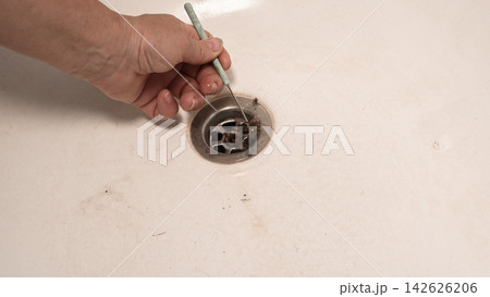 worker cleans clogged drain in sink using small metal tool. worker cleans clogged drain in sink using small metal tool. 142626206