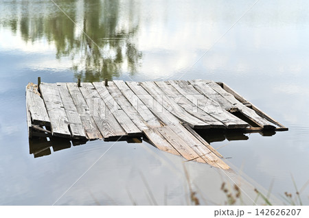 Wooden pier floating on calm lake water with tree reflection. Wooden pier floating on calm lake water with tree reflection. 142626207