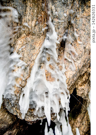Ice icicles hanging on stone surface of cave, frozen water lake Baikal in winter Ice icicles hanging on stone surface of cave, frozen water lake Baikal in winter 142626331