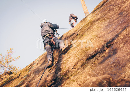 Rock climber climbing high rock wall, extreme sport outside, alpinism equipment Rock climber climbing high rock wall, extreme sport outside, alpinism equipment 142626425
