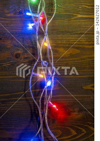 Colorful LED Christmas fairy lights glowing on a dark brown wooden plank background, creating a festive holiday atmosphere. Abstract holiday illumination and decoration background Colorful LED Christmas fairy lights glowing on a dark brown wooden plank background, creating a festive holiday atmosphere. Abstract holiday illumination and decoration background 142627012