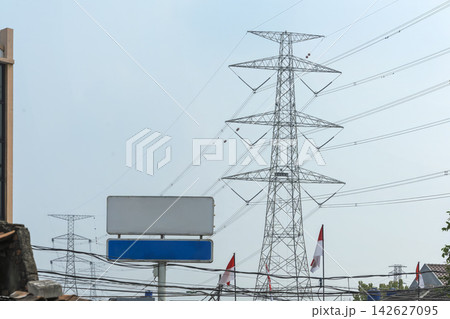 High voltage electricity transmission tower and power lines behind a blank street sign and Indonesian flags. Concept of the electricity energy industry High voltage electricity transmission tower and power lines behind a blank street sign and Indonesian flags. Concept of the electricity energy industry 142627095