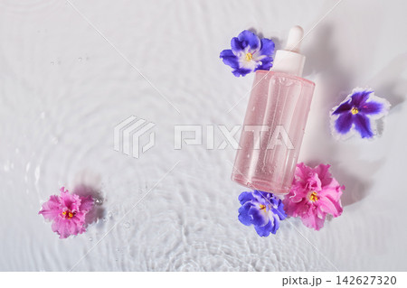 Skincare bottle with serum and fresh flowers floating on water with ripples Skincare bottle with serum and fresh flowers floating on water with ripples 142627320
