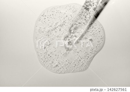 Transparent cosmetic serum with bubbles spilling from glass pipette, creating clear gel puddle Transparent cosmetic serum with bubbles spilling from glass pipette, creating clear gel puddle 142627561