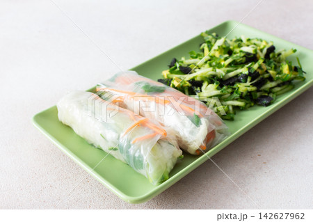 Rolls with red fish, carrots, and cucumbers in rice paper sit next to a fresh salad with cucumbers and avocado. This meal is great for breakfast or lunch and is gluten-free Rolls with red fish, carrots, and cucumbers in rice paper sit next to a fresh salad with cucumbers and avocado. This meal is great for breakfast or lunch and is gluten-free 142627962