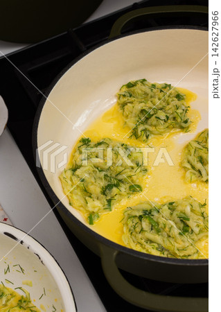 Zucchini pancakes are being prepared in a pan on the stove. A bowl of pancake batter sits nearby. The kitchen has basic tools and a clean countertop Zucchini pancakes are being prepared in a pan on the stove. A bowl of pancake batter sits nearby. The kitchen has basic tools and a clean countertop 142627966