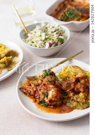 Plates hold amaranth, millet, and quinoa porridge served with baked white hake in tomato sauce. Fresh salad is beside the porridge. A bowl of kiwi sits nearby for dessert 142627984