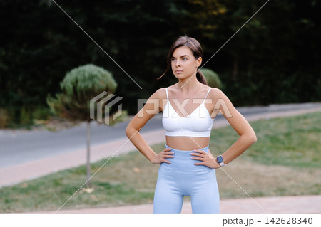 Confident sportswoman posing with hands on hips in a park Confident sportswoman posing with hands on hips in a park 142628340